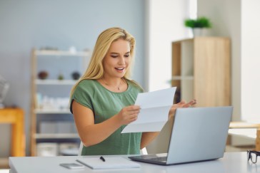 Woman looking at paper sitting in front of laptop