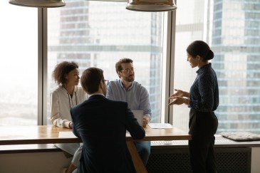 Group of employees listening to standing female employee speak
