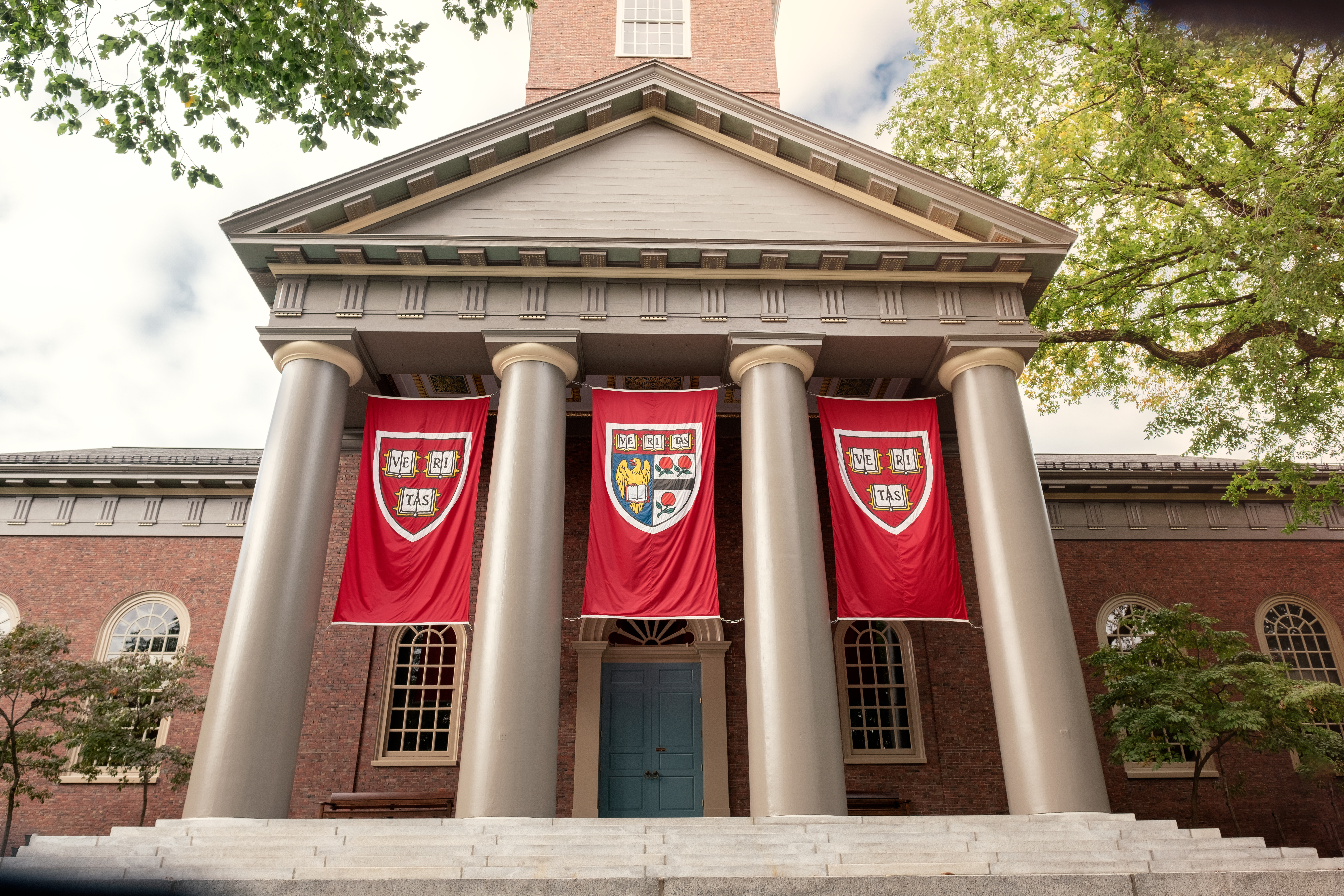 Harvard University campus: A building with four pillars and three Harvard emblem flags hanging between them.