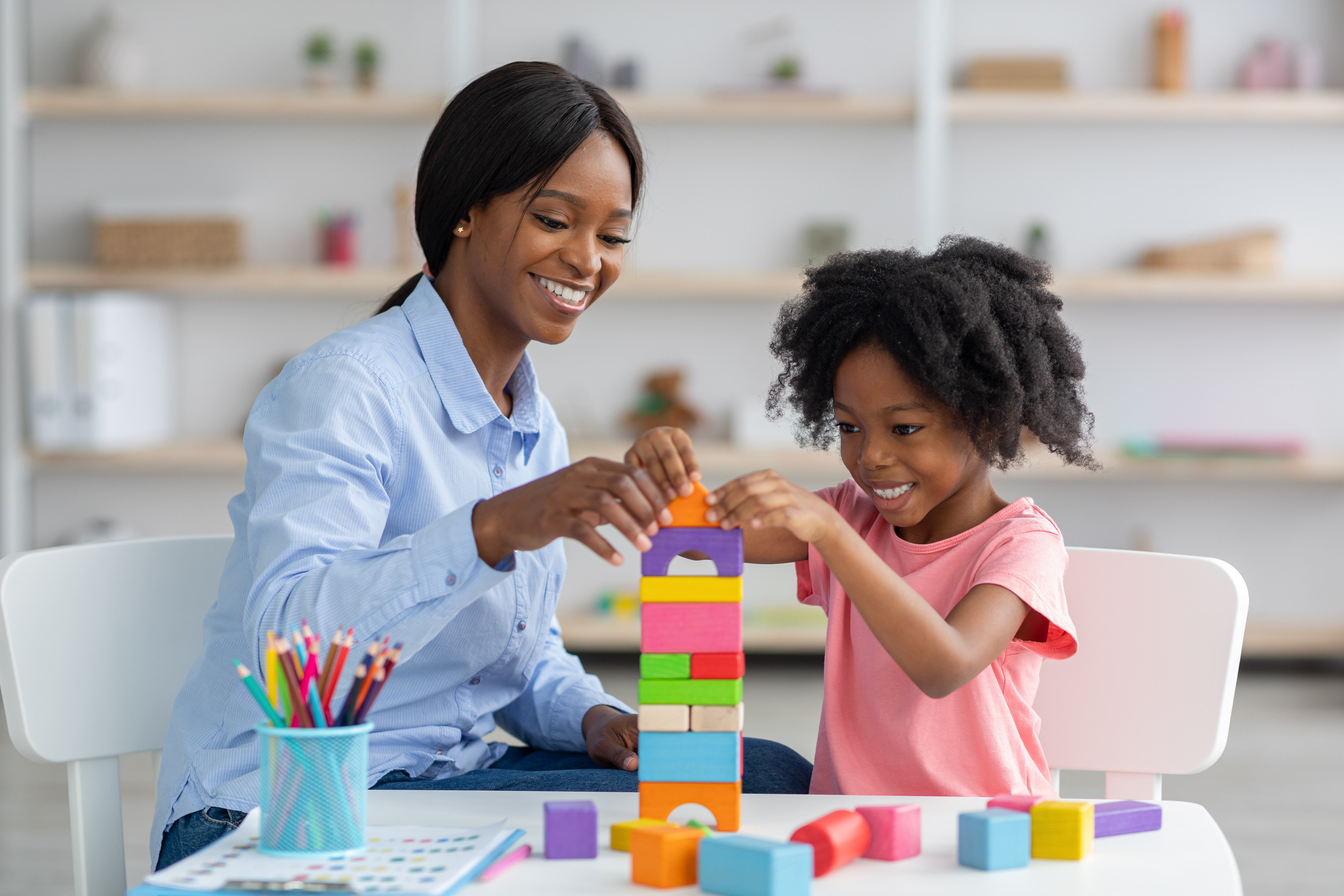 A woman helps a child stack colorful blocks on top of round white table.