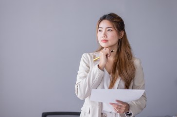 Woman holding pen and paper, thinking
