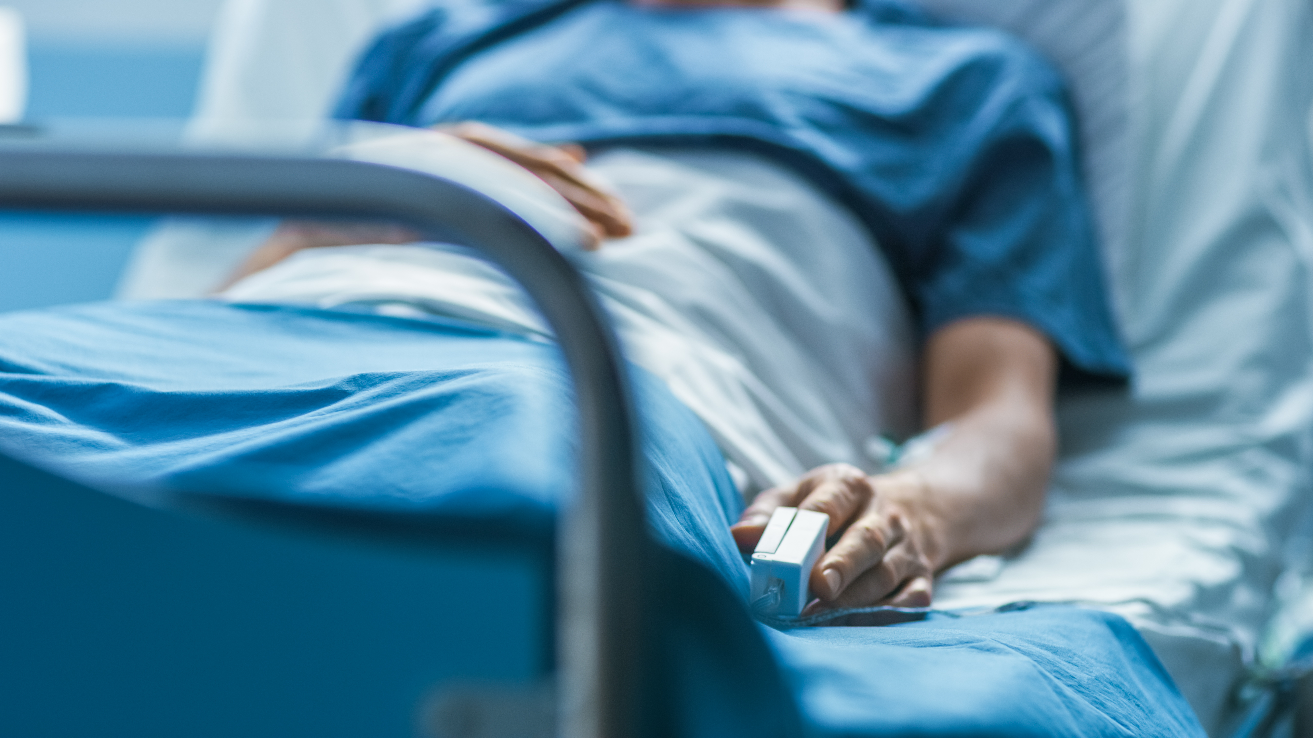 A person lying down on a hospital bed, dressed in a blue hospital gown.