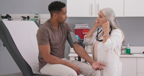 Female doctor with stethoscope talking to male patient in exam room