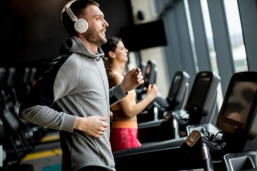 Man wearing headphones jogging on treadmill at gym