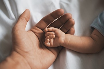 A baby's small hands rest in their father's hand.