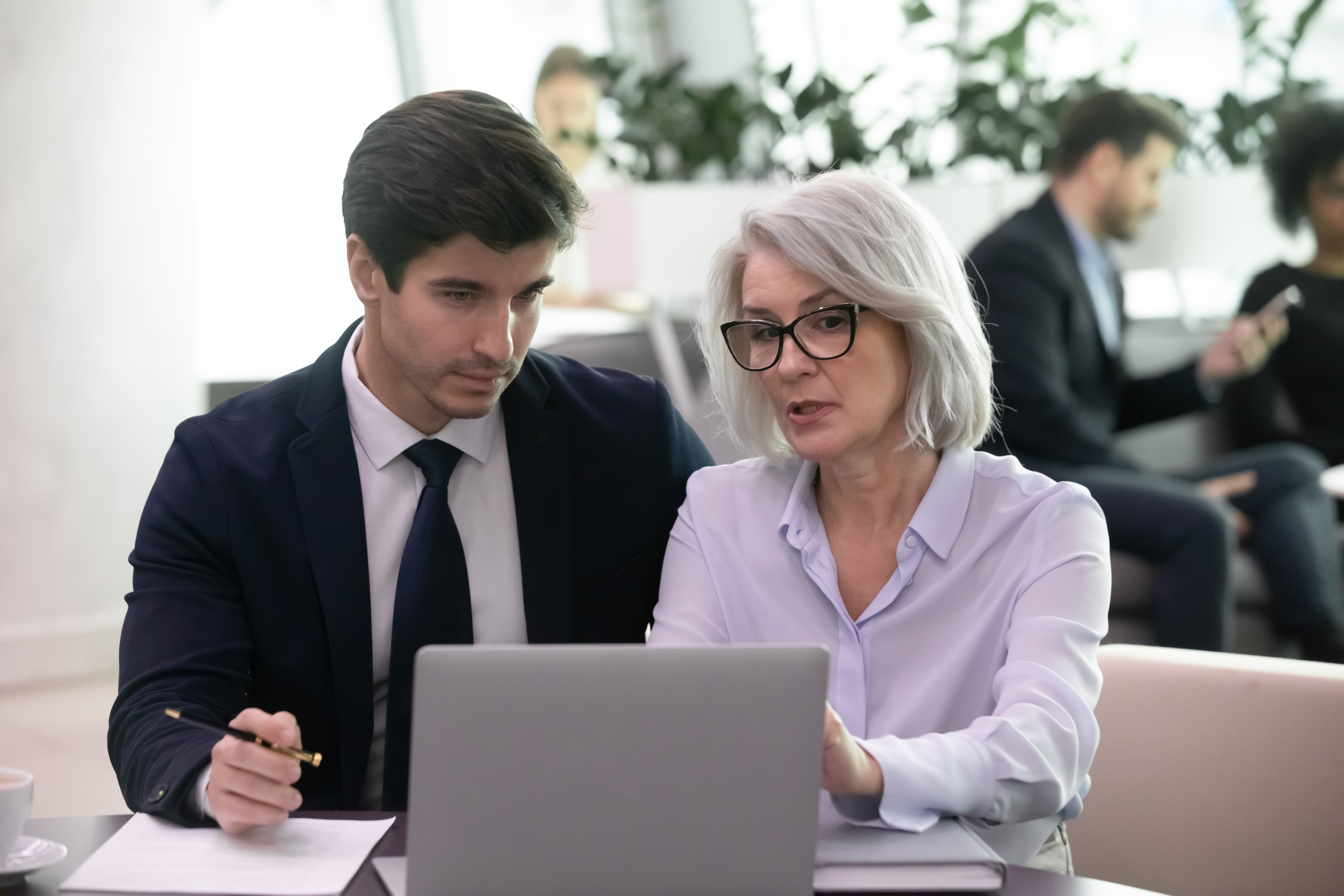 Older female and younger male employee looking at laptop working together