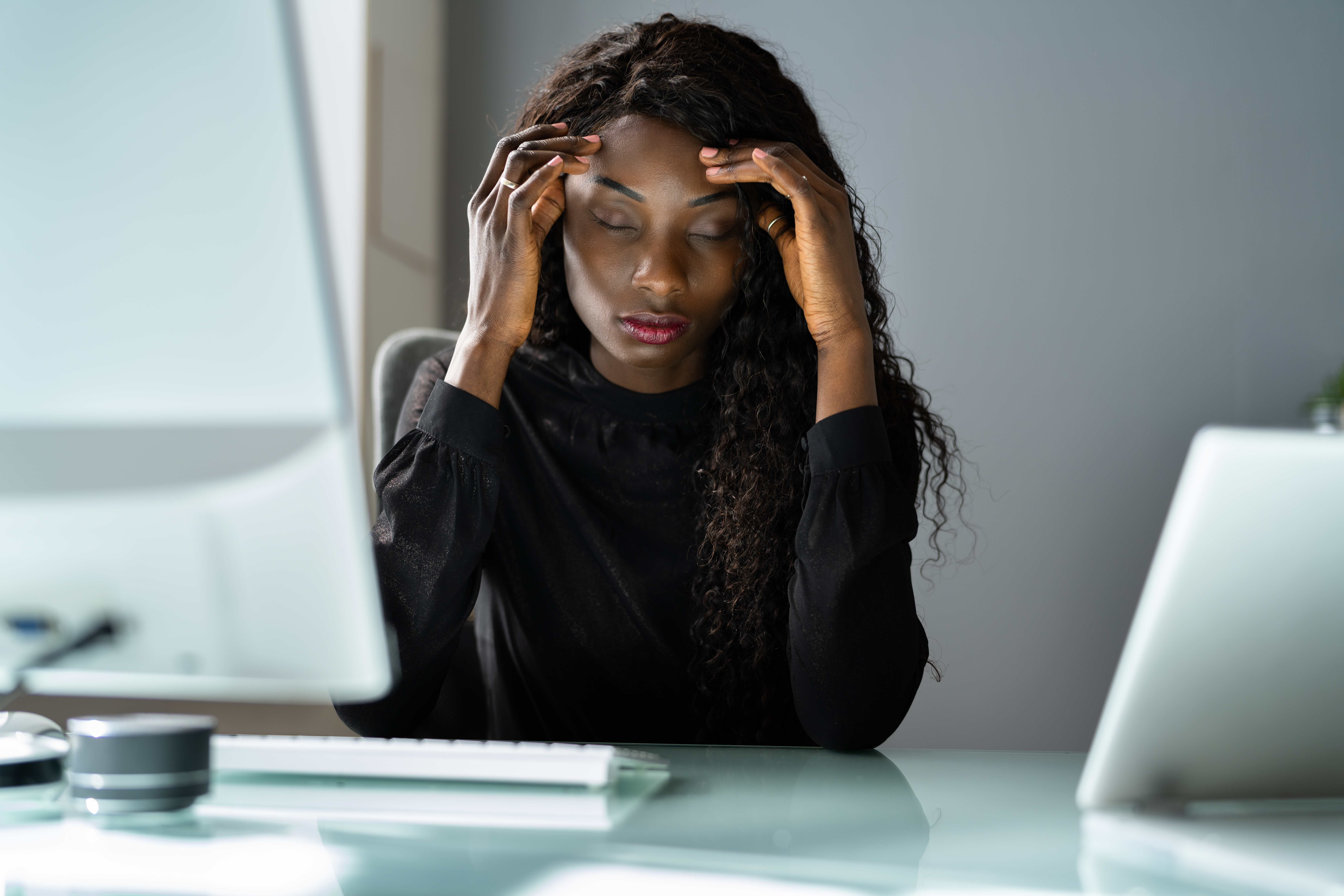 Woman sitting at desk holding head; stressed