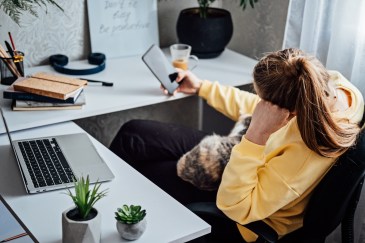 A woman at her desk, faced away from her laptop while looking at her phone.