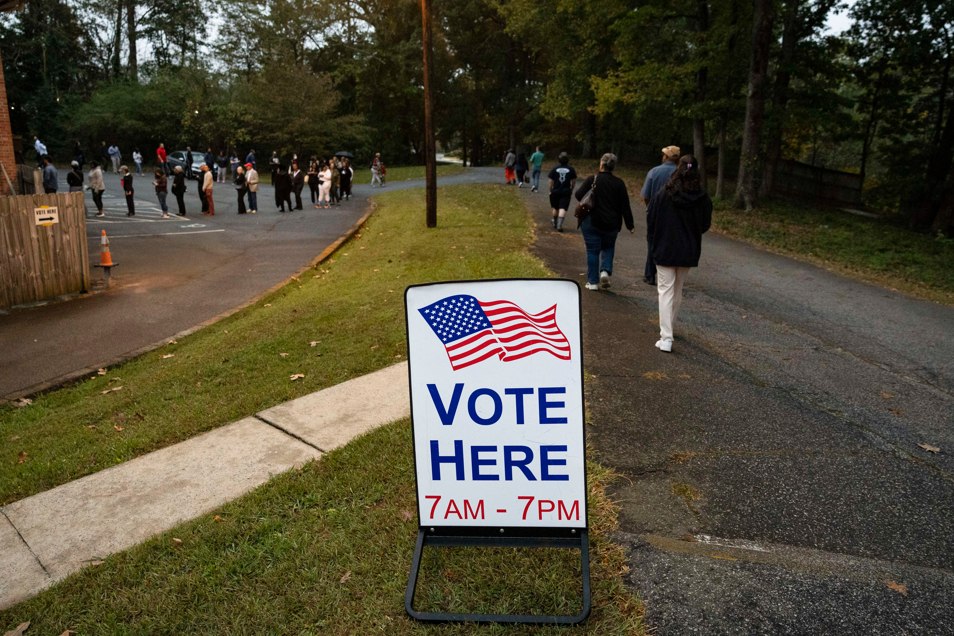People line up near a sign that reads "Vote Here."