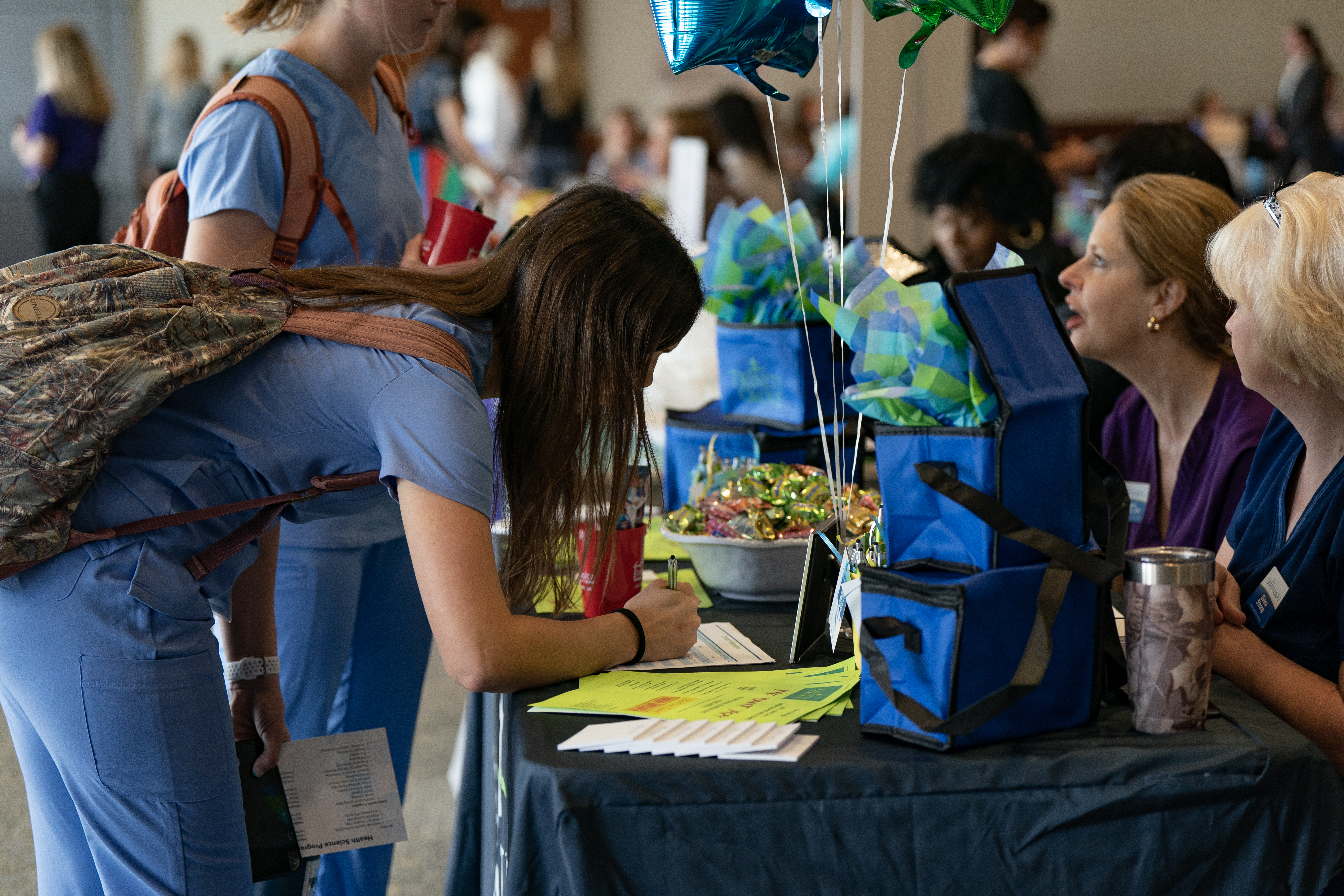 A college student is writing on a piece of paper on a table at what looks like a job fair.