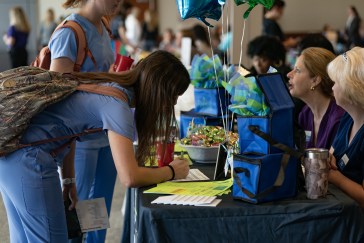 A college student is writing on a piece of paper on a table at what looks like a job fair.