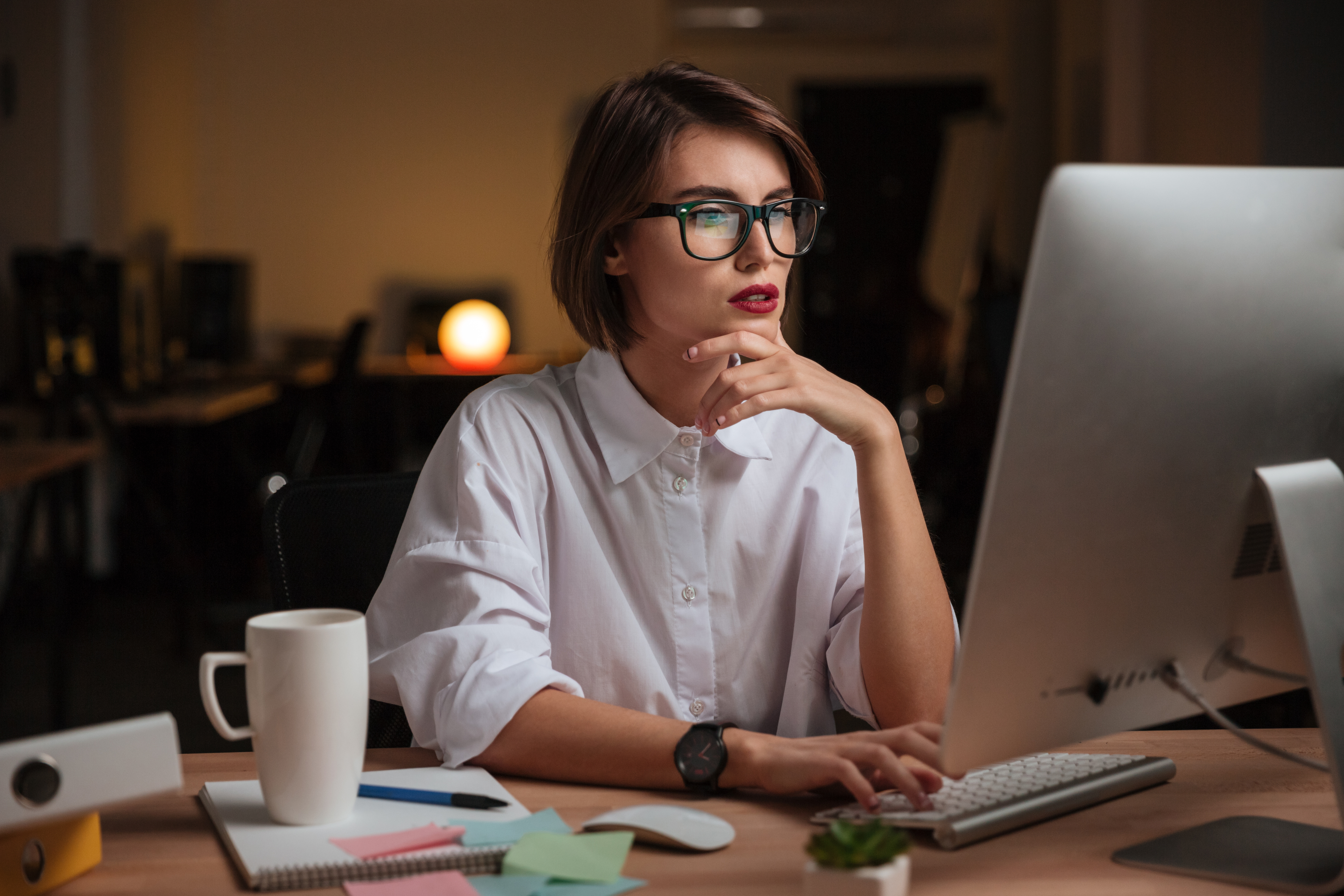 Woman wearing glasses working on desktop with coffee cup