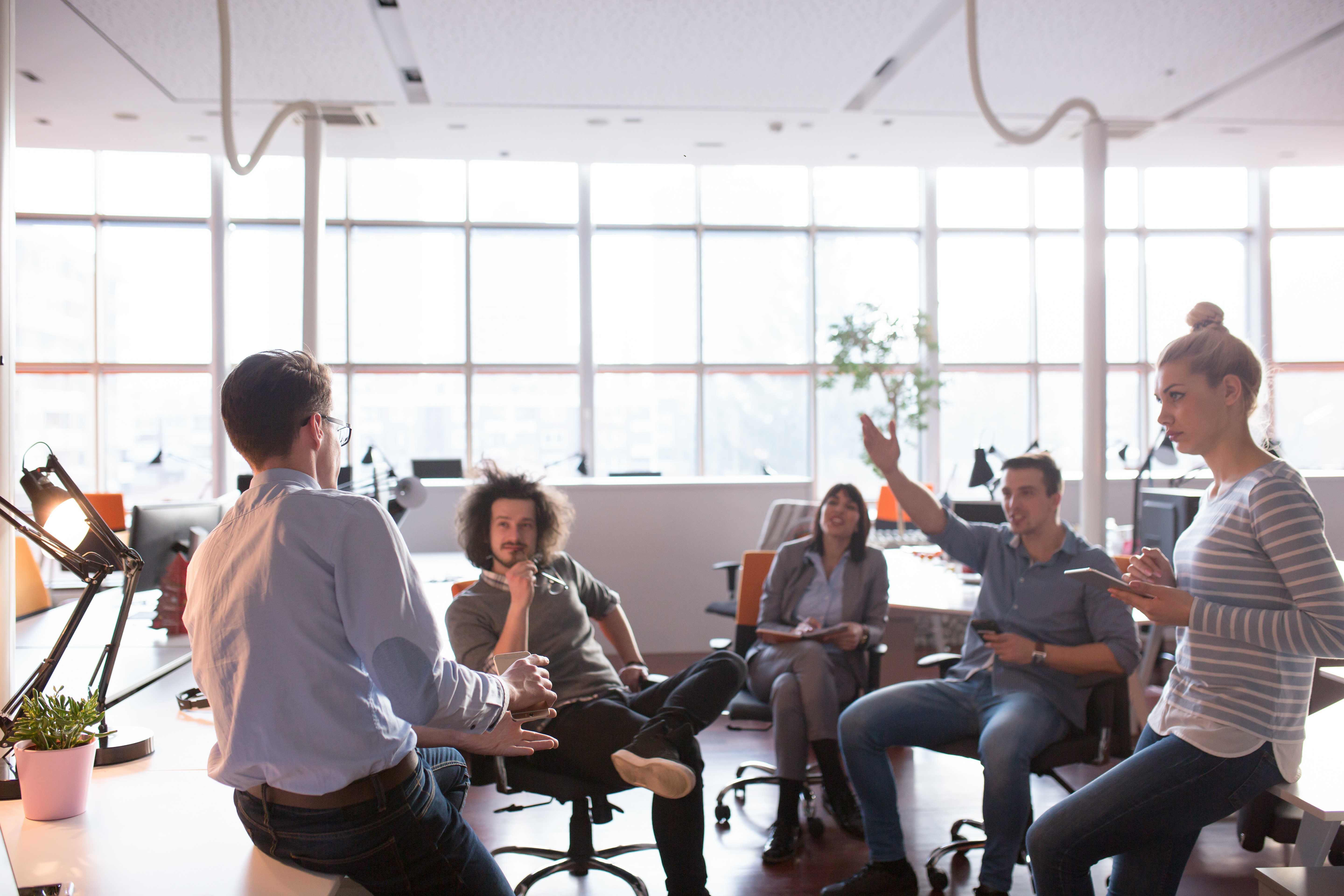 Group of employees talking in circle in office, one raising hand