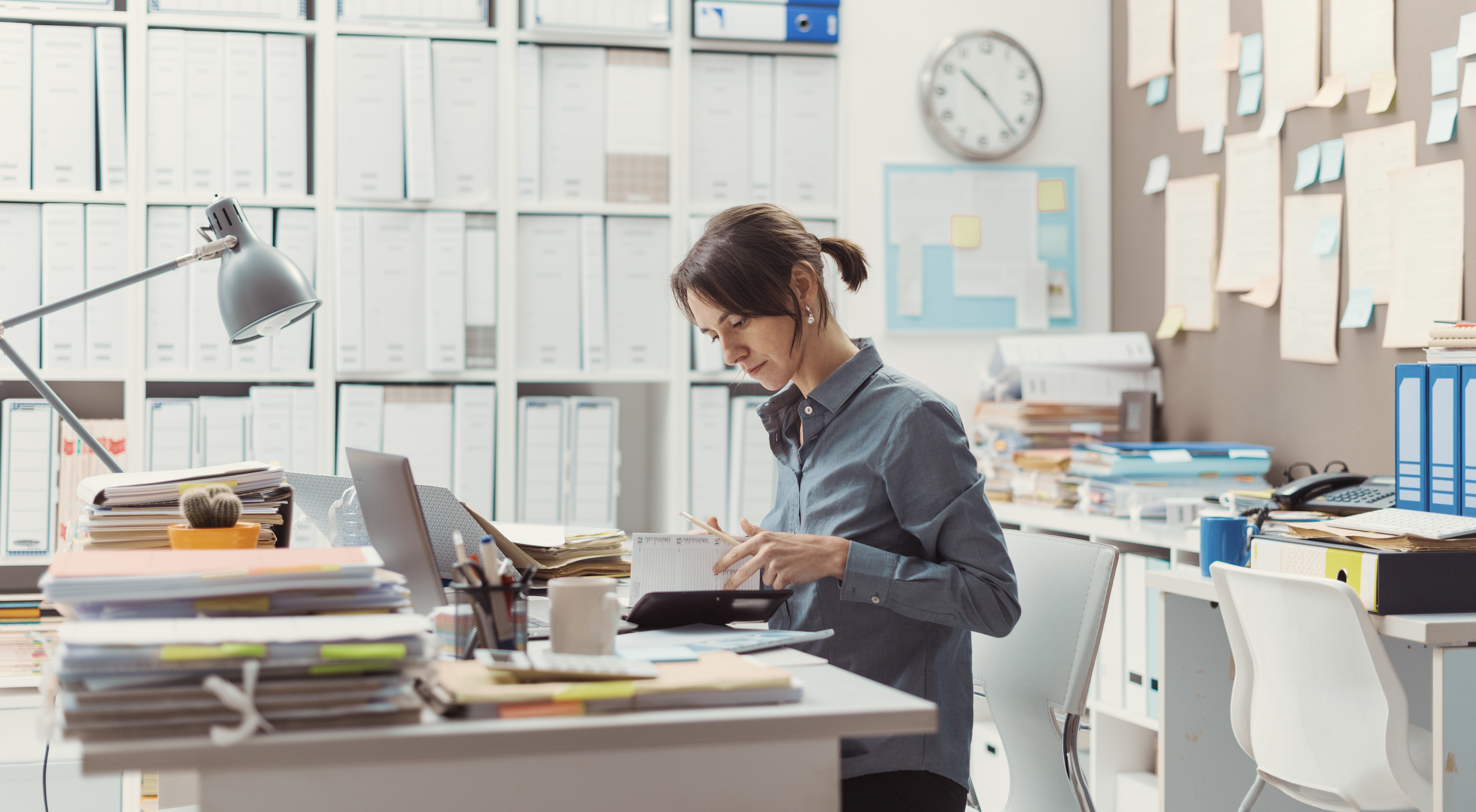 Woman sitting at desk surrounded by files, papers, computer, busy