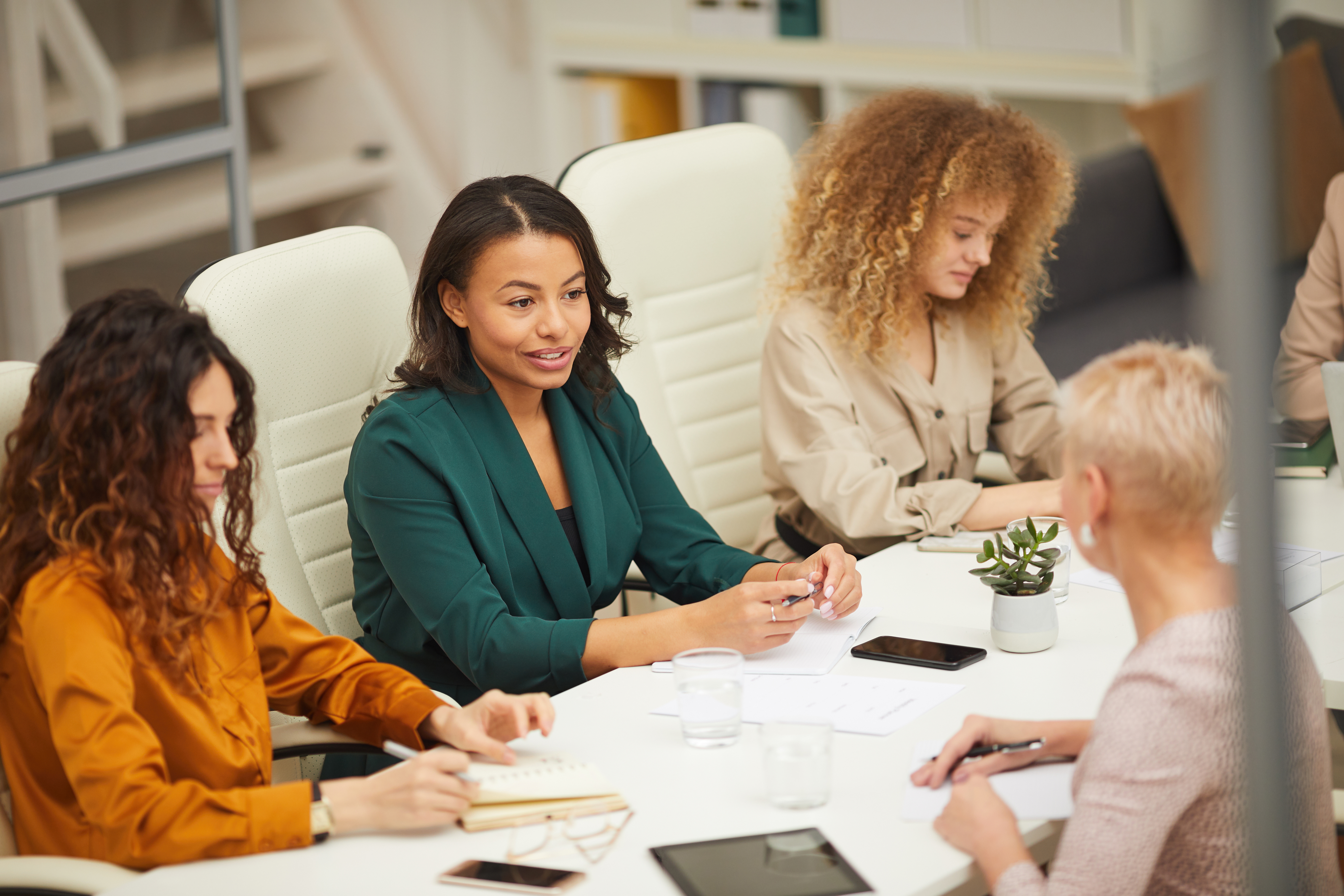 A group of women at a conference table with tablets, phones and papers.