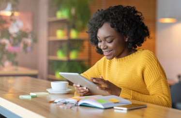 Woman sitting reading on tablet with teacup and book