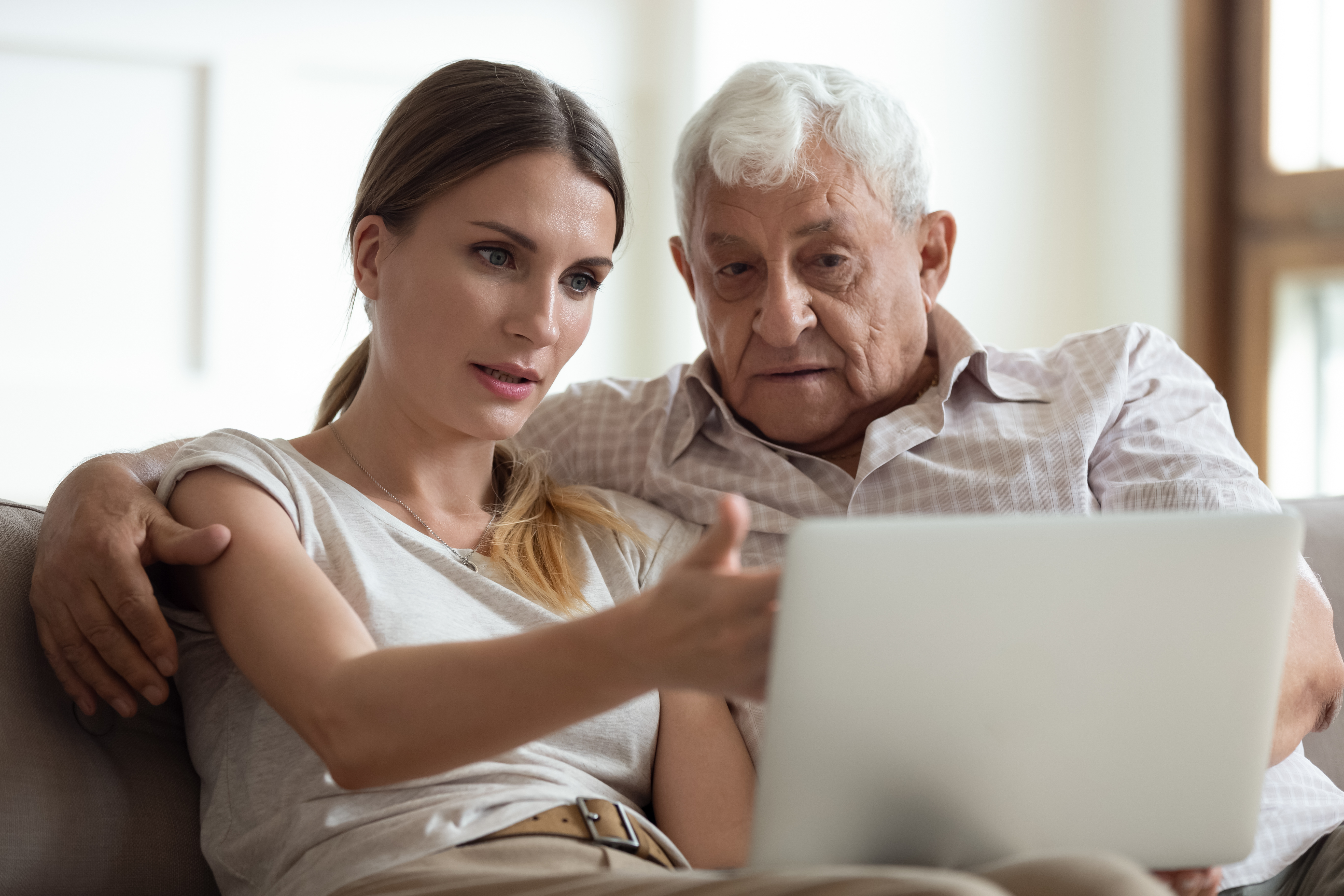 Younger woman and older man sitting on couch looking at laptop together