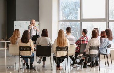 Woman teaching class of adults, standing at front of seated group