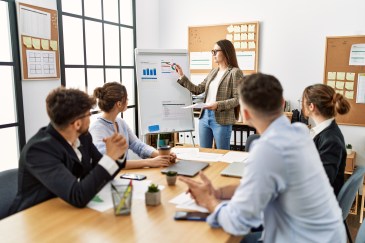 Group of employees in a meeting, woman standing pointing at chart