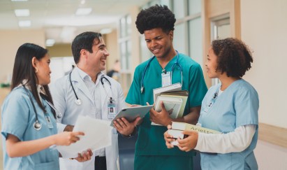 Group of young medical professionals standing, smiling, talking, holding books and looking at tablet