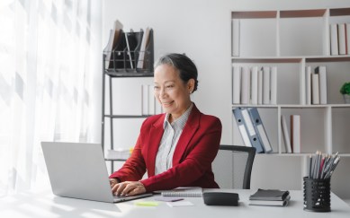 Female employee sitting at desk in office smiling, typing on laptop