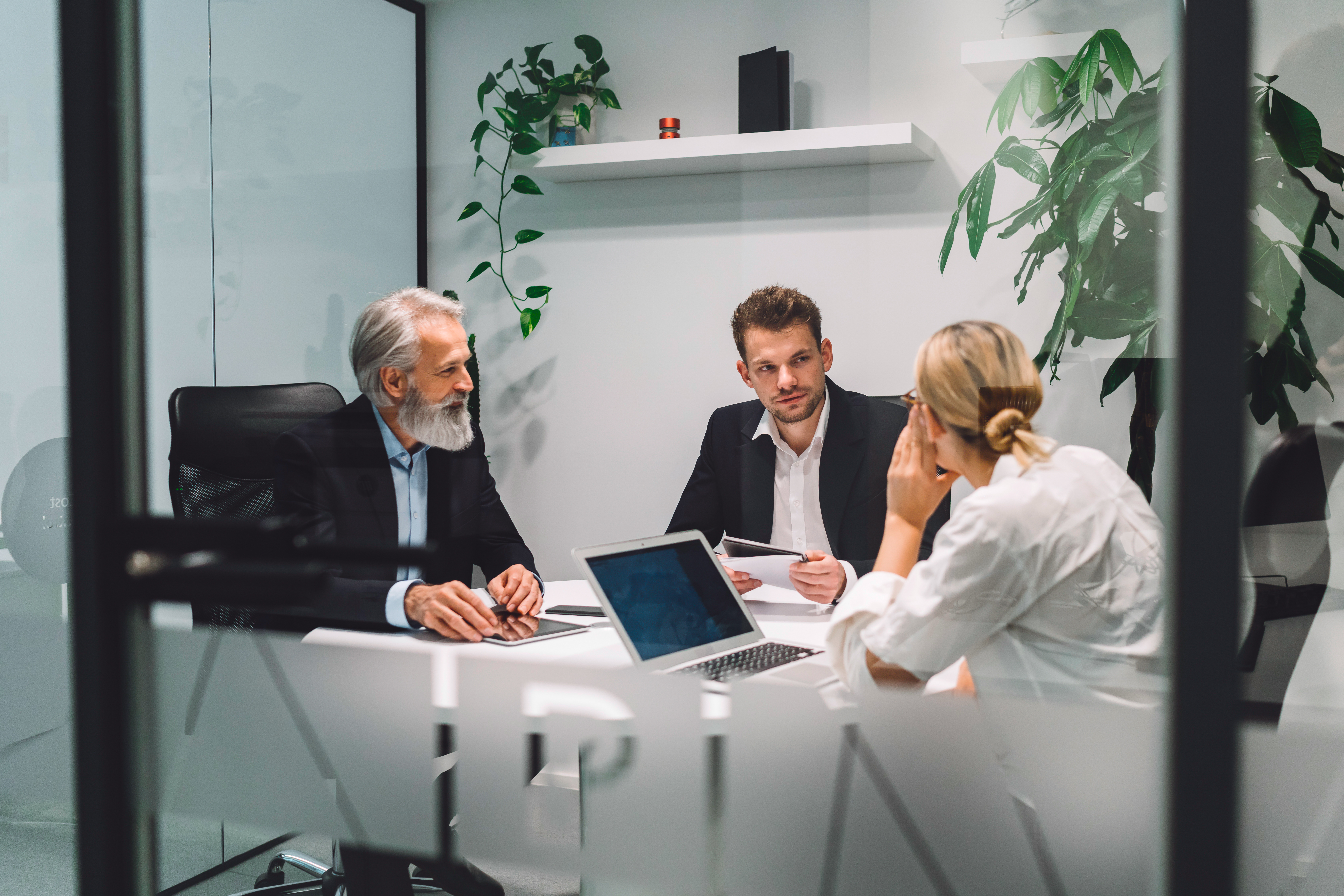 Older male and younger male and female employee sitting around table working in an office