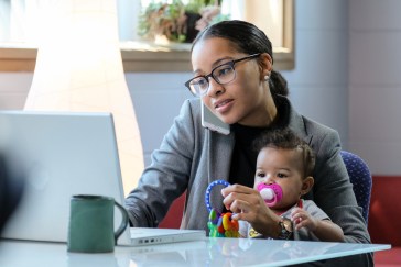 Woman sitting at computer with baby in her lap, on phone