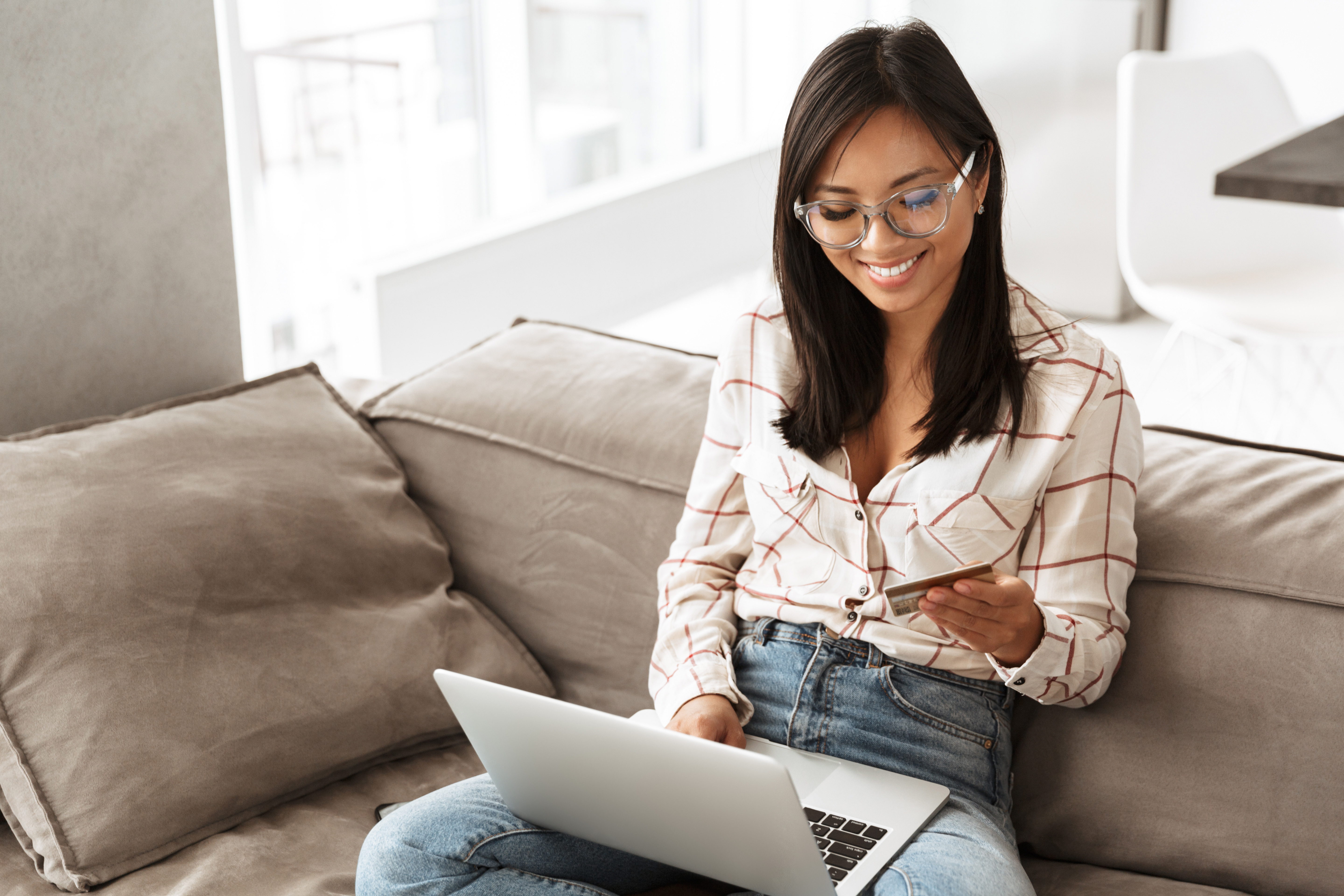 Woman working on laptop, sitting on couch, smiling, looking at credit card