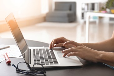 Person typing on laptop; glasses sitting on desk