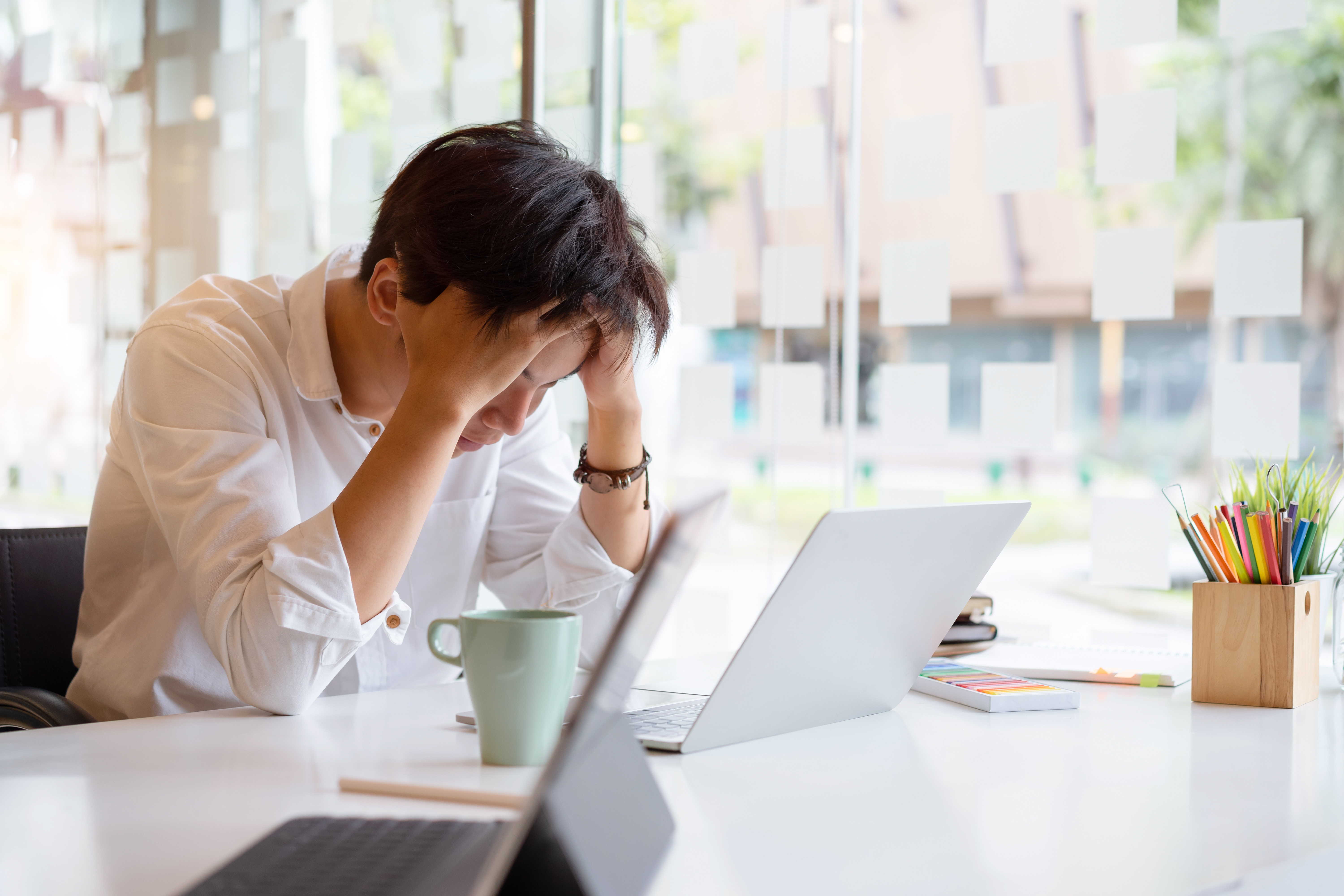 A young man has his head in his hands while looking down at his laptop.