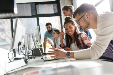 Young employees working together at long desk with computers