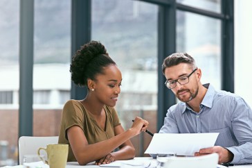 Male and female employees working together at table, looking at paper