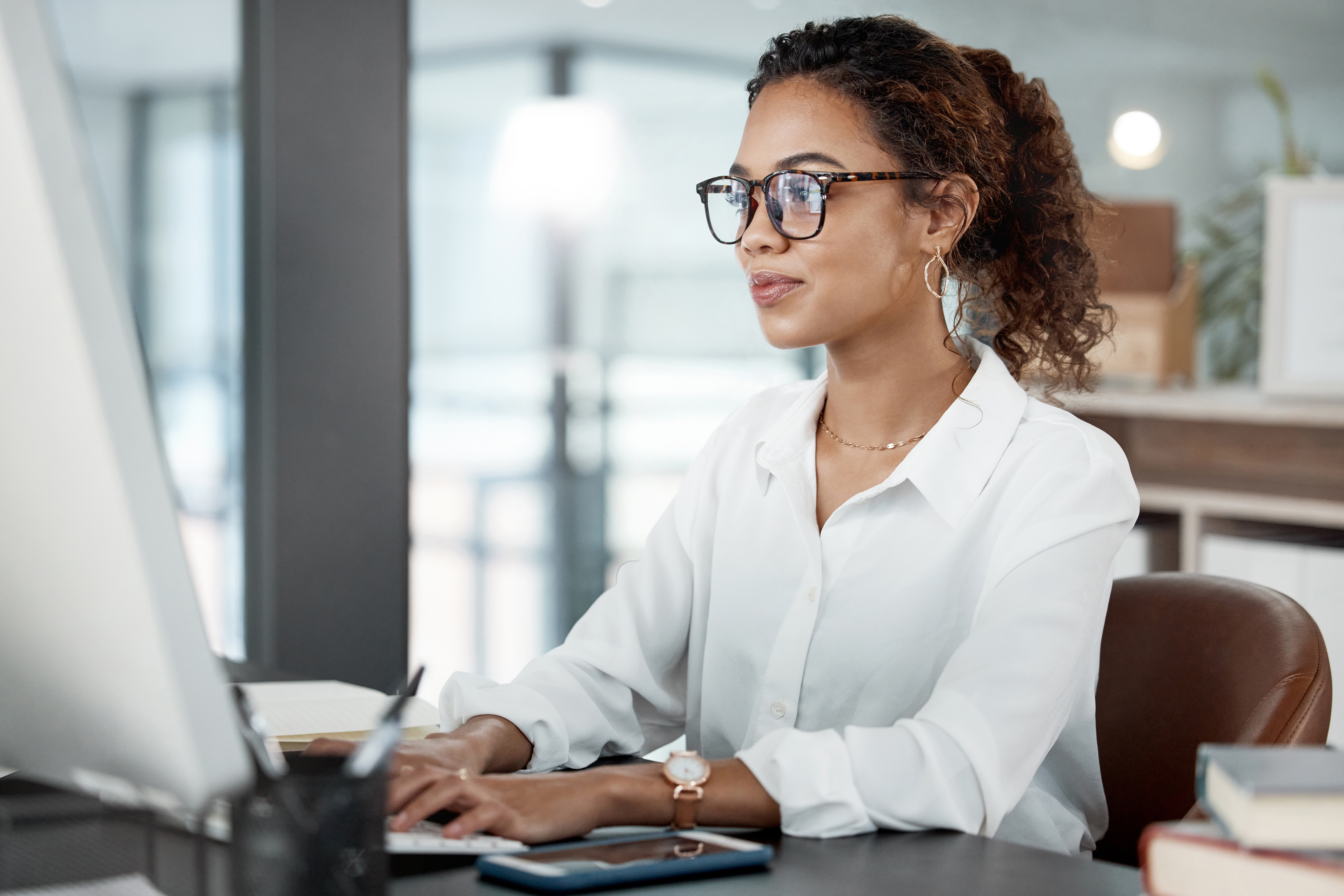 Woman wearing glasses and white shirt sitting at computer typing