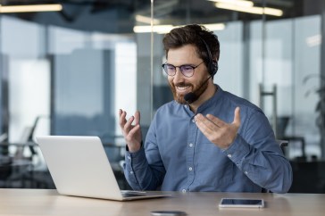 Man with headset speaking with someone on laptop in office