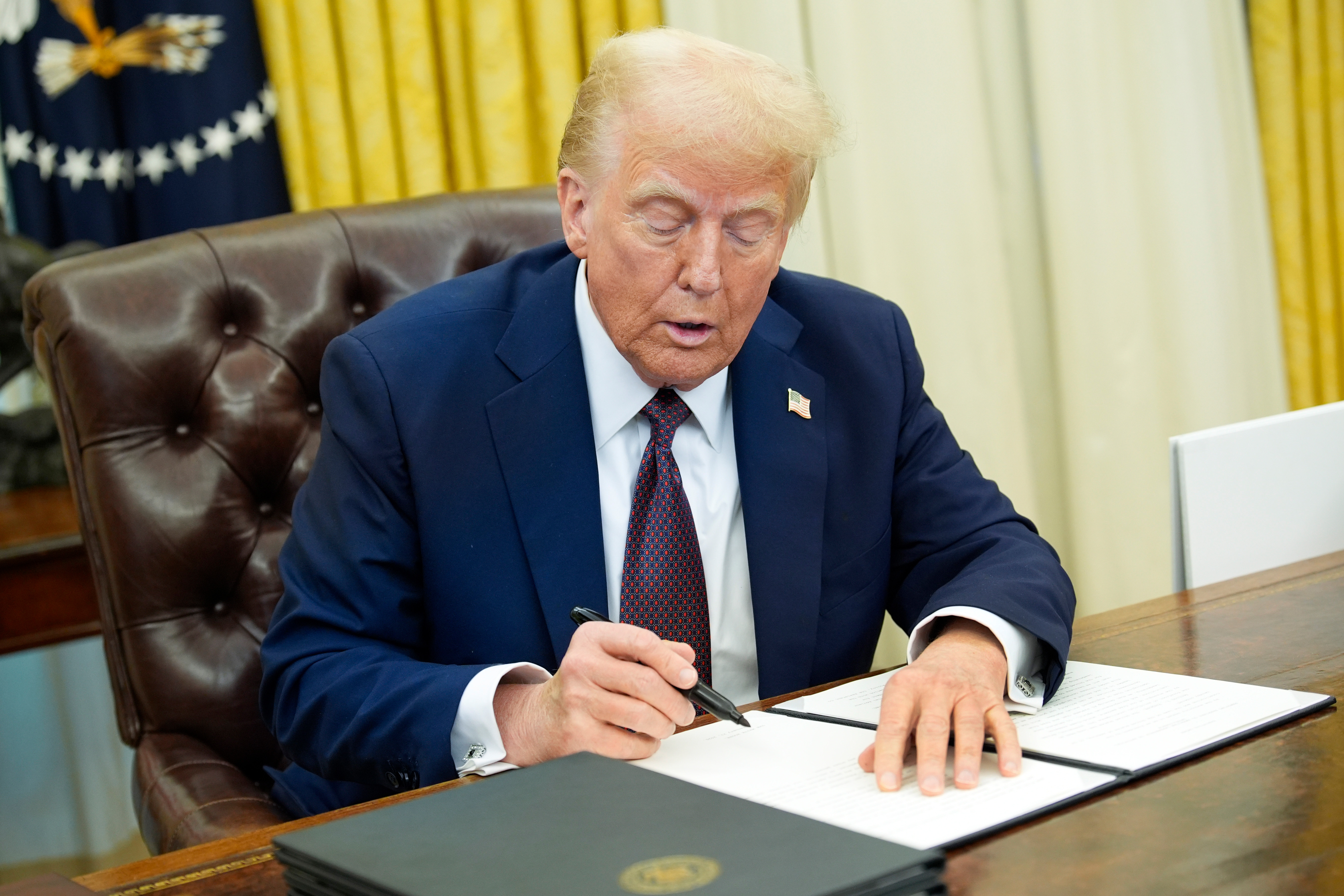 US President Donald Trump signs an executive order in the Oval Office.