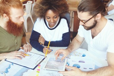 Three people working together around table with charts and papers
