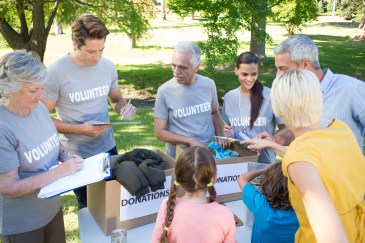 Group of people wearing volunteer shirts standing at table with donation boxes