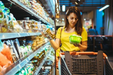 A woman looks at two items while standing in a grocery aisle.