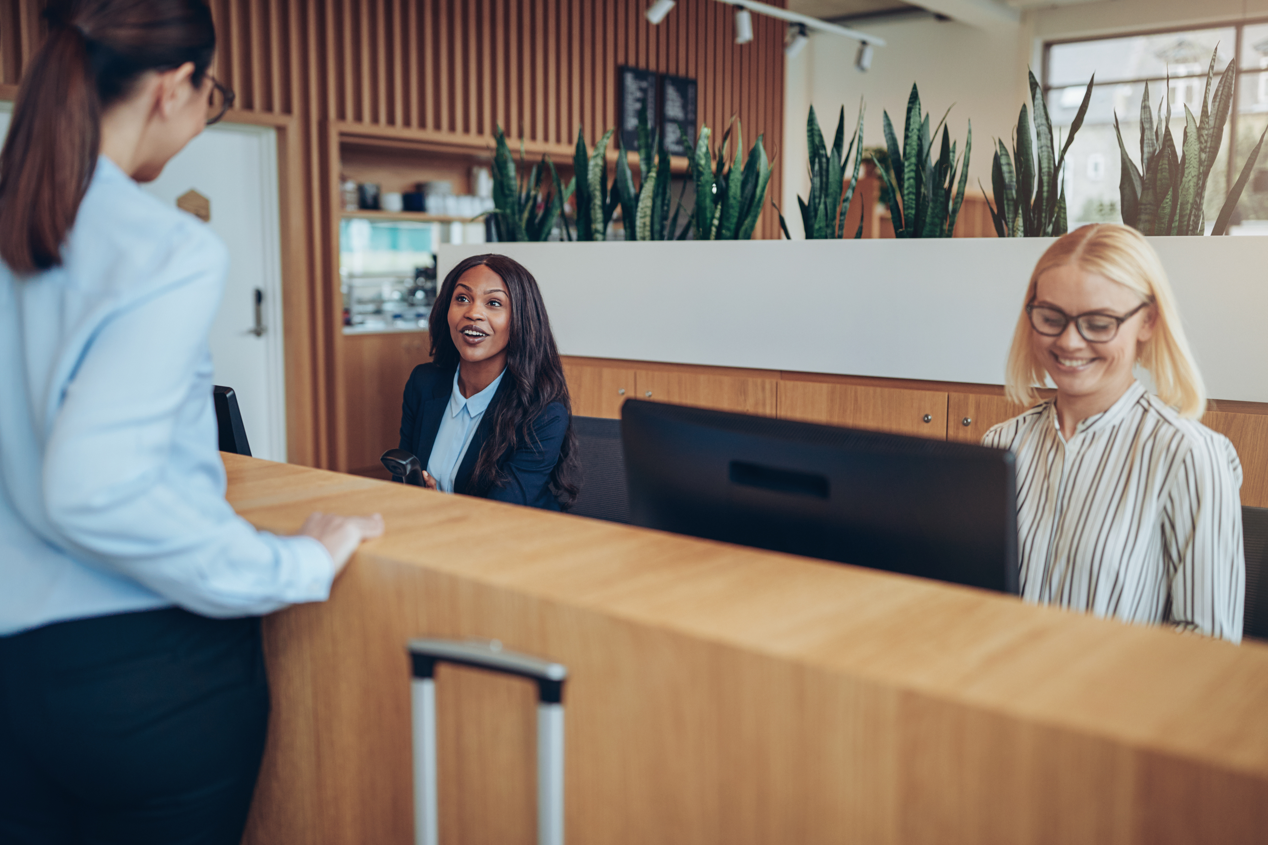 Hotel employees sitting behind desk; hotel guest speaking to woman behind desk