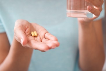 Woman's hands holding two pills and a cup of water