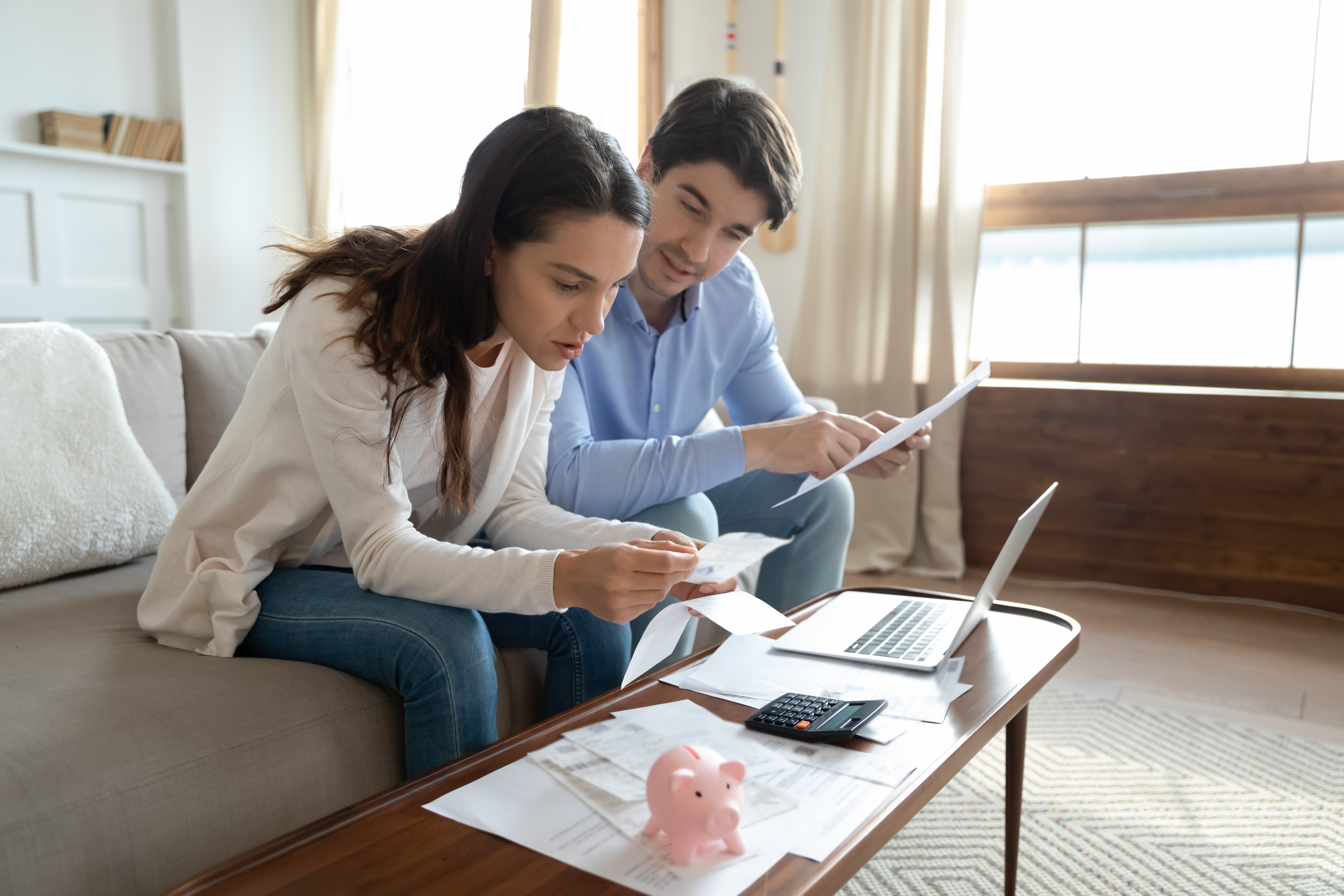 Couple looking at paperwork, woman working on computer, small piggybank on table