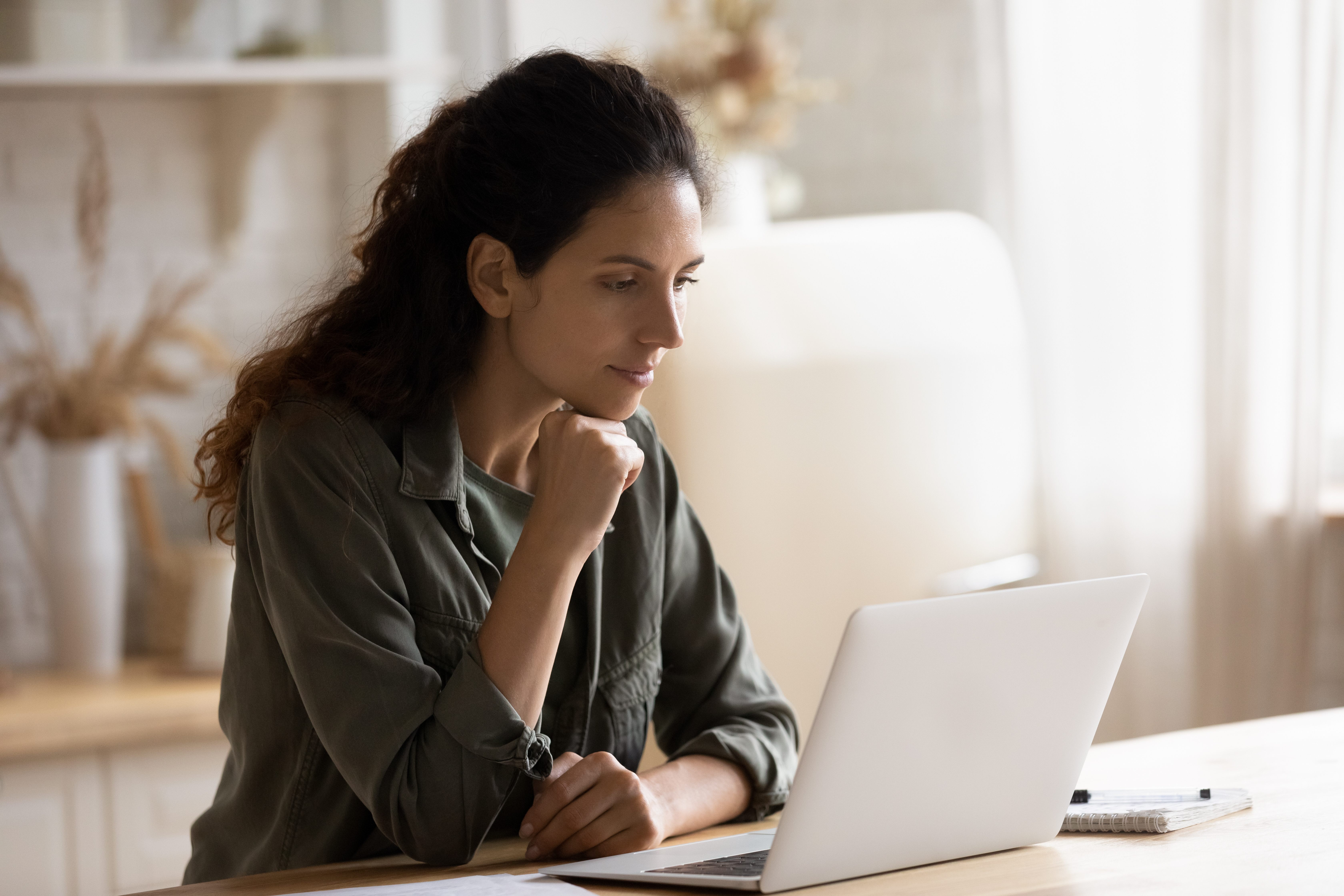 Woman with dark, curly hair sitting at counter looking at laptop