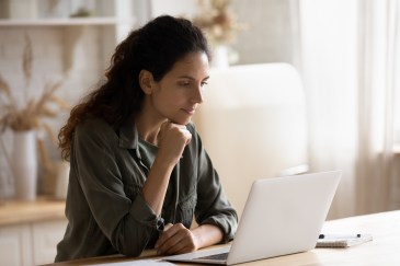 Woman with dark, curly hair sitting at counter looking at laptop