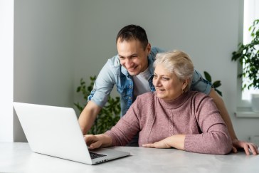 Younger man helping older woman on laptop computer