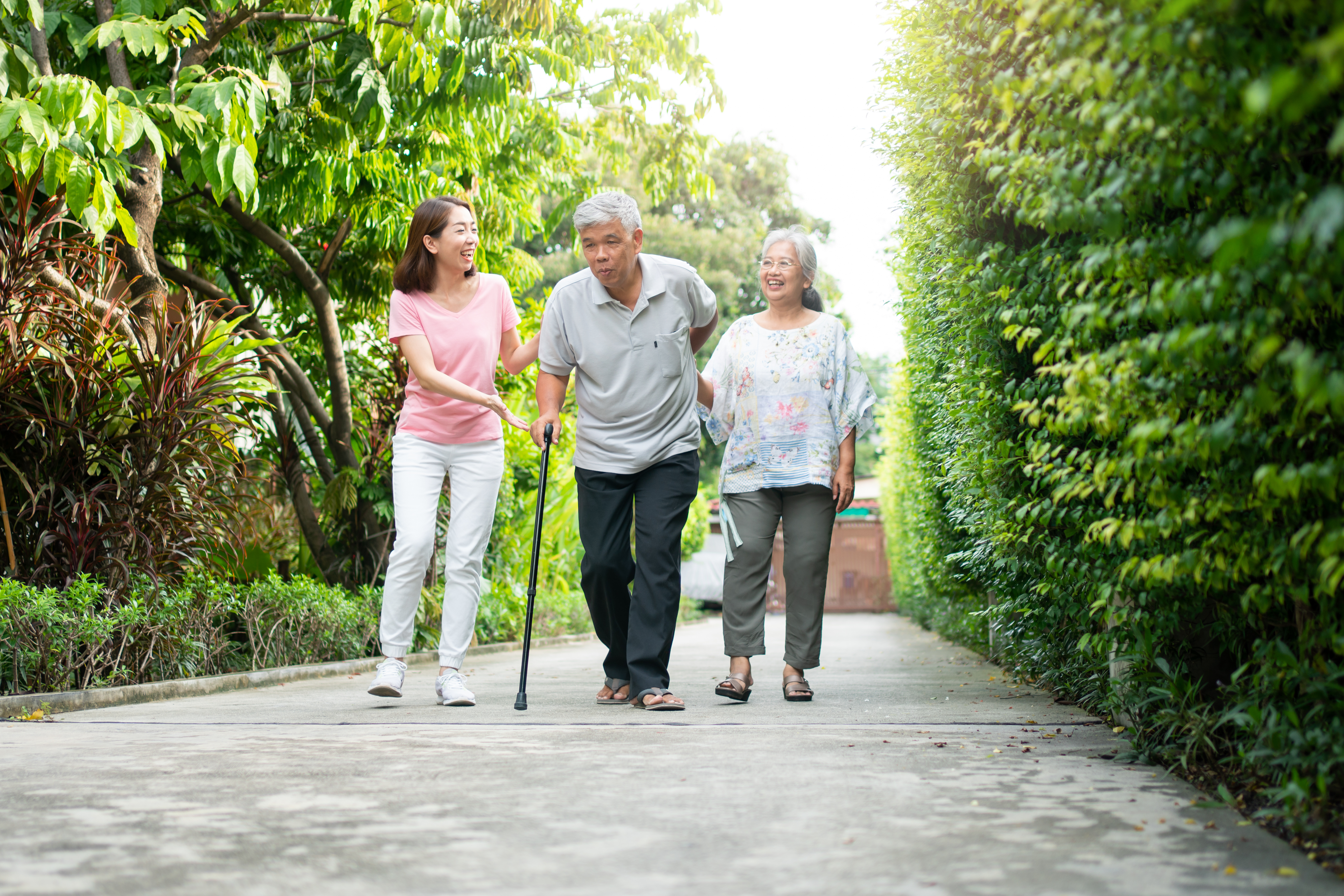 Younger woman walking with aging couple, parents, older man using cane