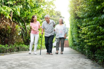 Younger woman walking with aging couple, parents, older man using cane