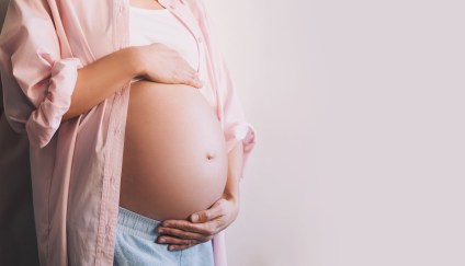 A woman wearing a flannel holds her pregnant belly.