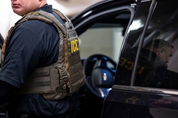 A U.S. Immigration and Customs Enforcement (ICE) officer enters a vehicle.