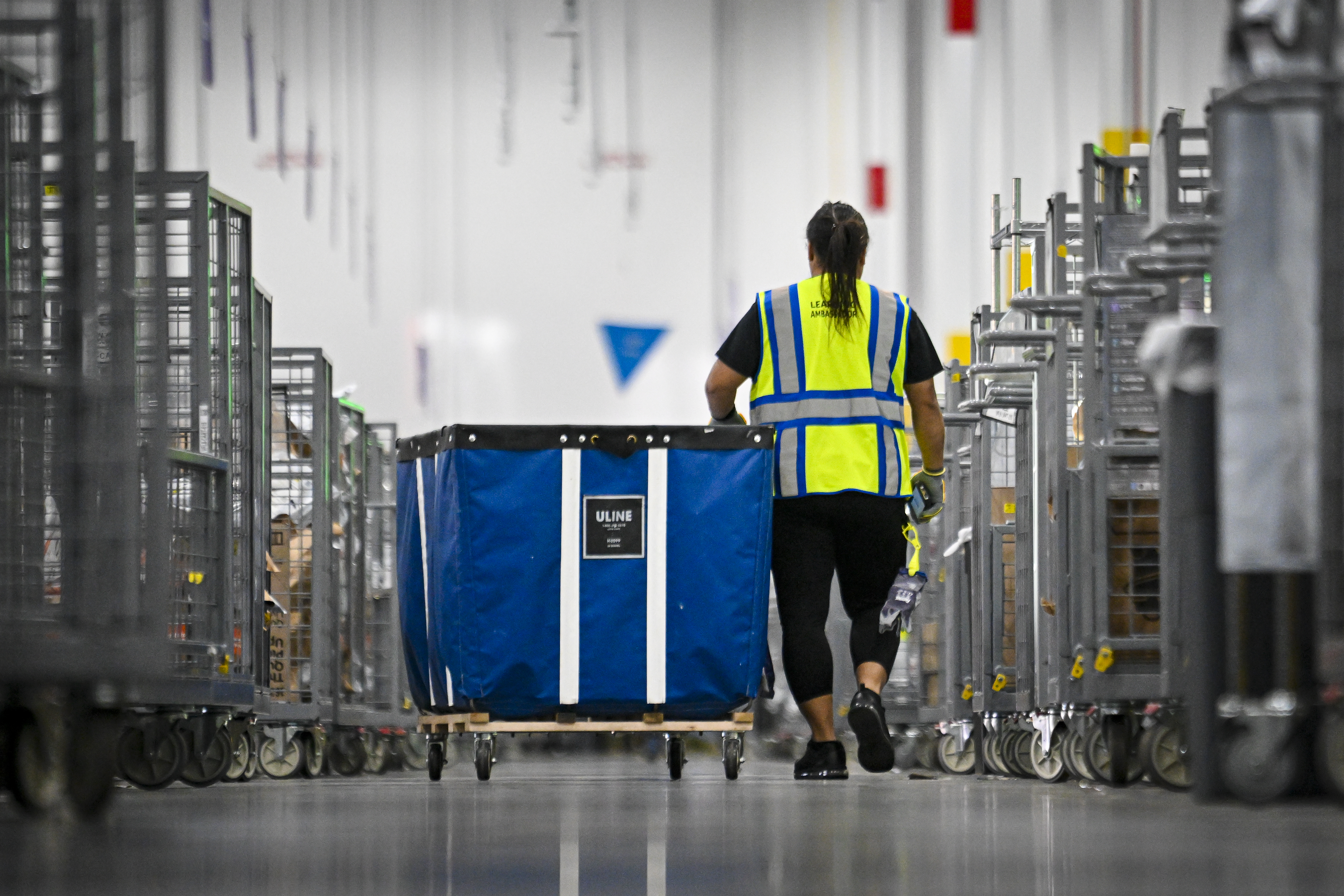 An Amazon worker pushes a blue bin through a warehouse.