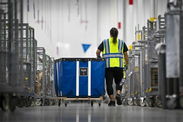 An Amazon worker pushes a blue bin through a warehouse.